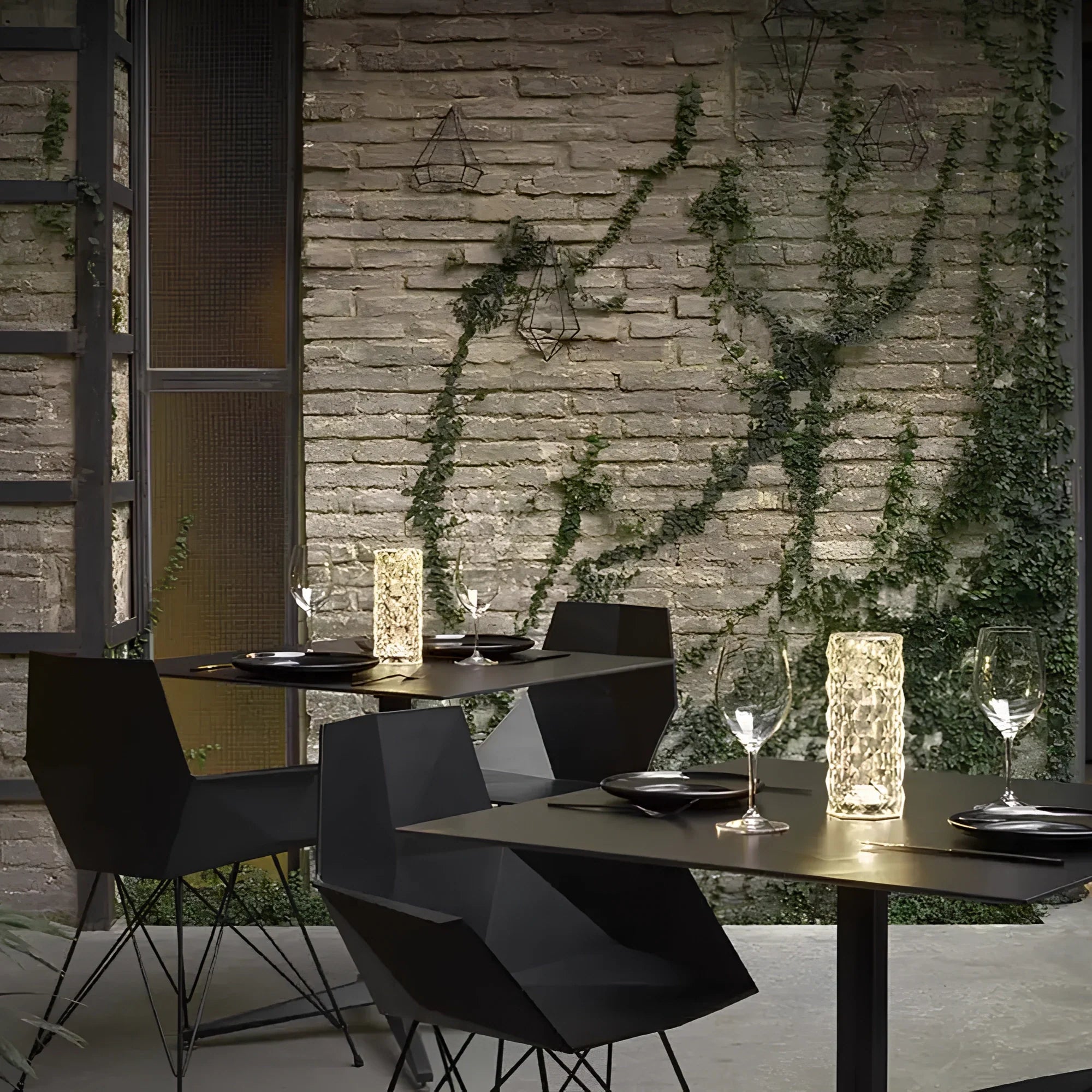 Modern dining setup with black chairs and tables against a stone wall with greenery.