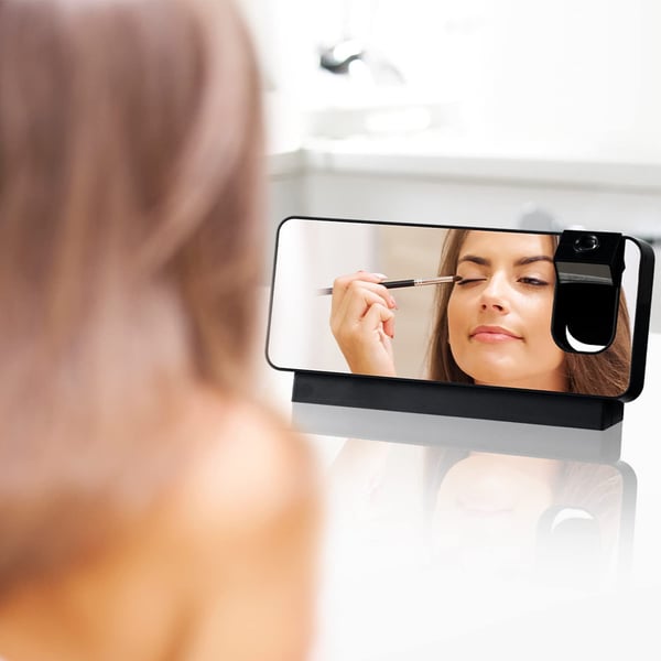 Person applying makeup with a smartphone displaying a mirror app.