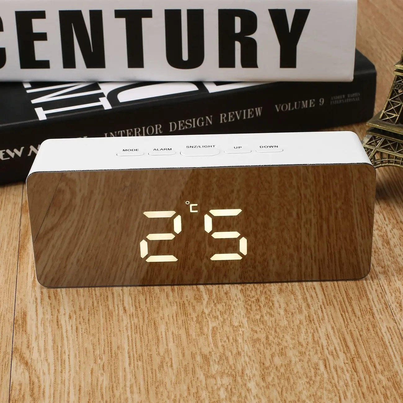 Wooden digital clock displaying temperature on a wooden surface with books in the background