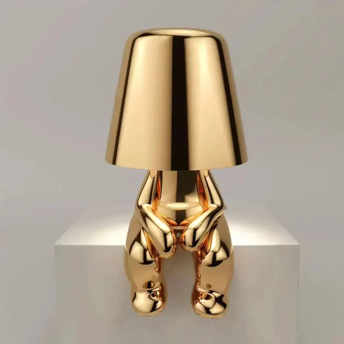 Gold-colored lamp with a unique design on a white pedestal against a gray background