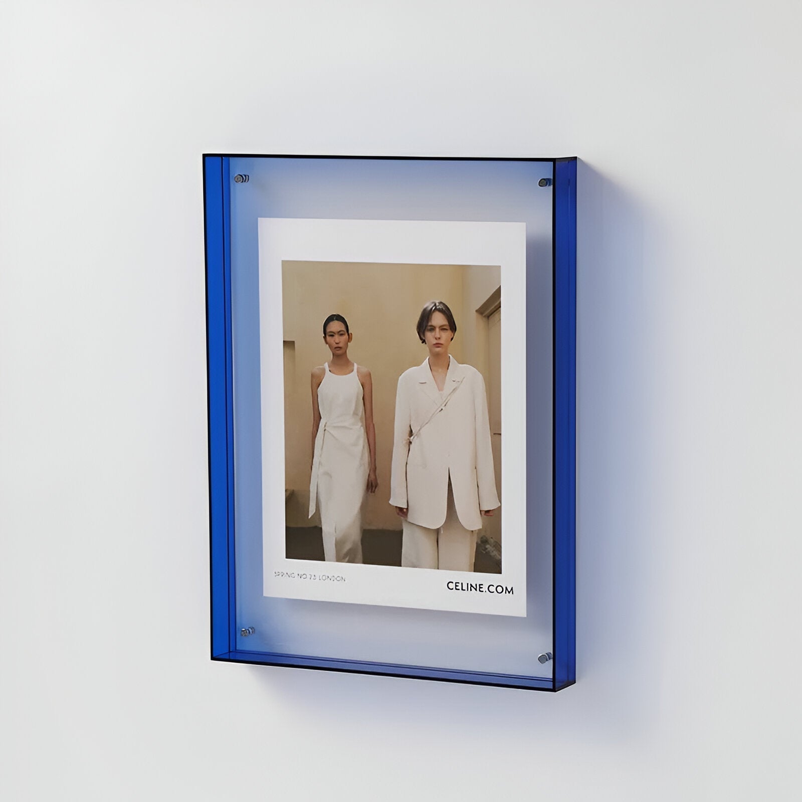 Framed photograph of two people in white outfits with a blue frame on a white wall.