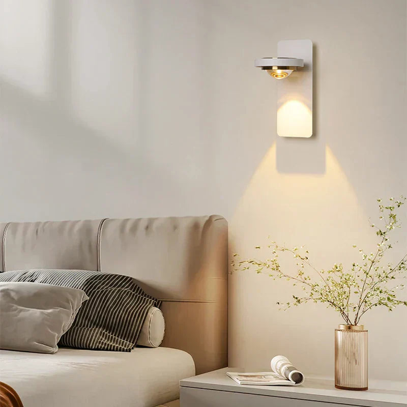 Modern wall sconce lighting fixture on a neutral wall above a sofa with decorative elements.