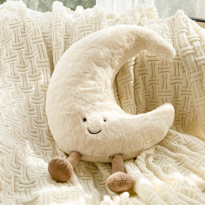 Plush moon-shaped pillow with a smiling face on a textured blanket