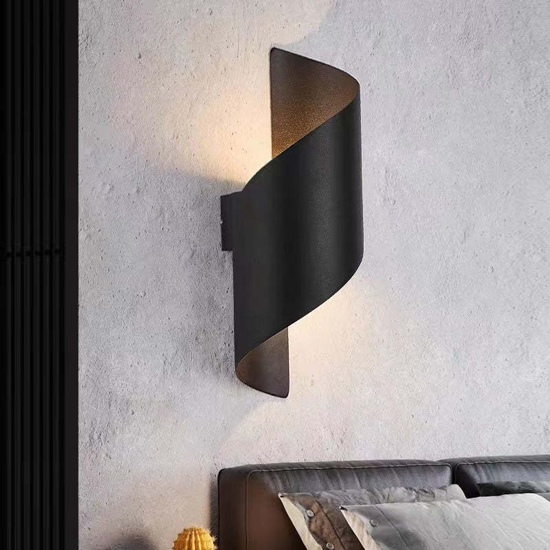 Modern black wall sconce on a textured wall above a bed.