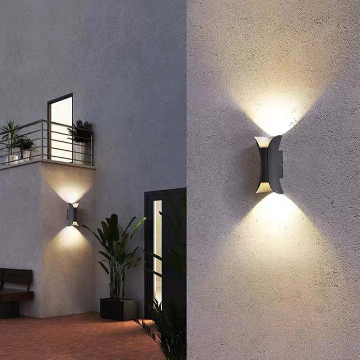Outdoor wall lights on a textured wall with plants and a bench.
