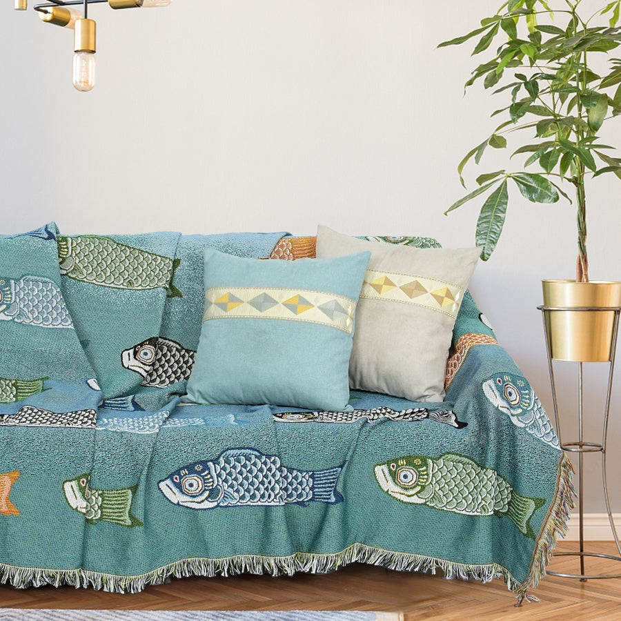 Teal fish-patterned throw blanket draped over a sofa with decorative pillows in a living room setting.