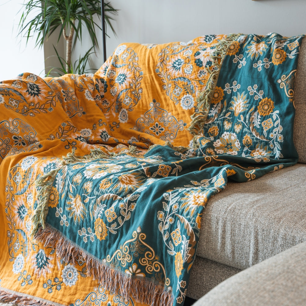 Floral patterned throw blanket draped over a sofa with a pillow.