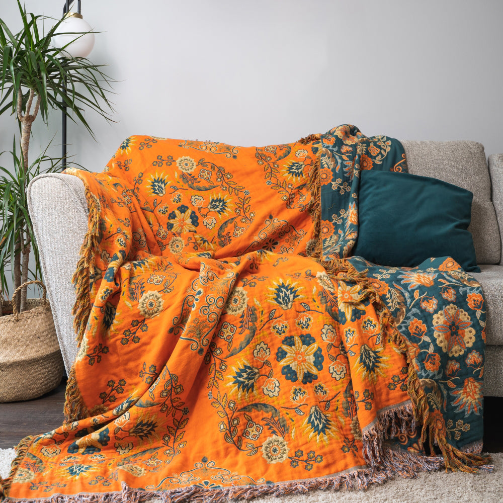 Orange and blue patterned throw blanket draped over a sofa with a plant in the background.