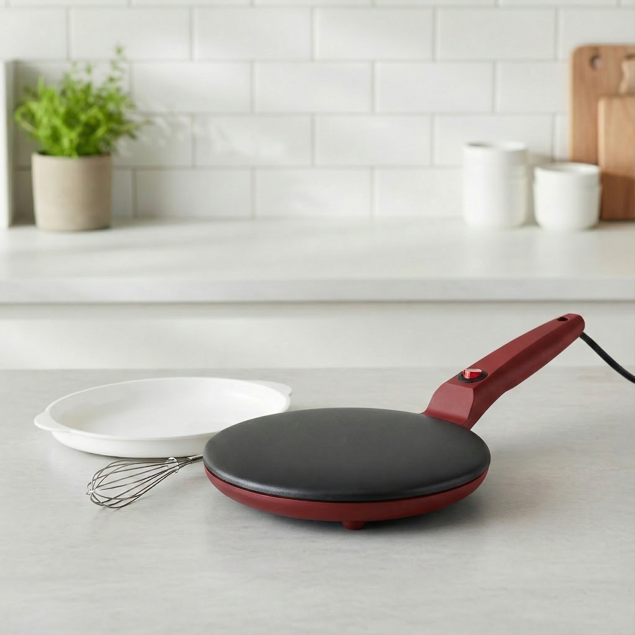 Red electric crepe maker on a kitchen counter with a white tiled wall in the background.
