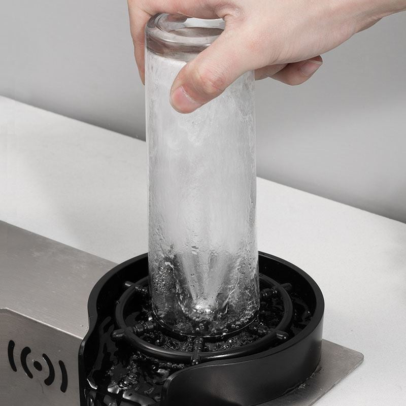 Hand placing a glass with ice into a black device on a white surface.