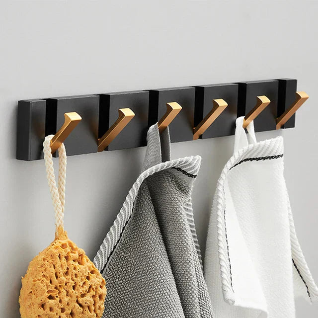 Black wall-mounted hook rack with gold hooks holding kitchen items on a gray wall.