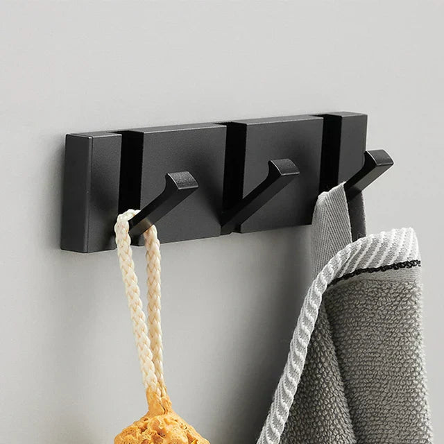 Black wall-mounted hook with three hooks holding a towel and a rope on a gray background
