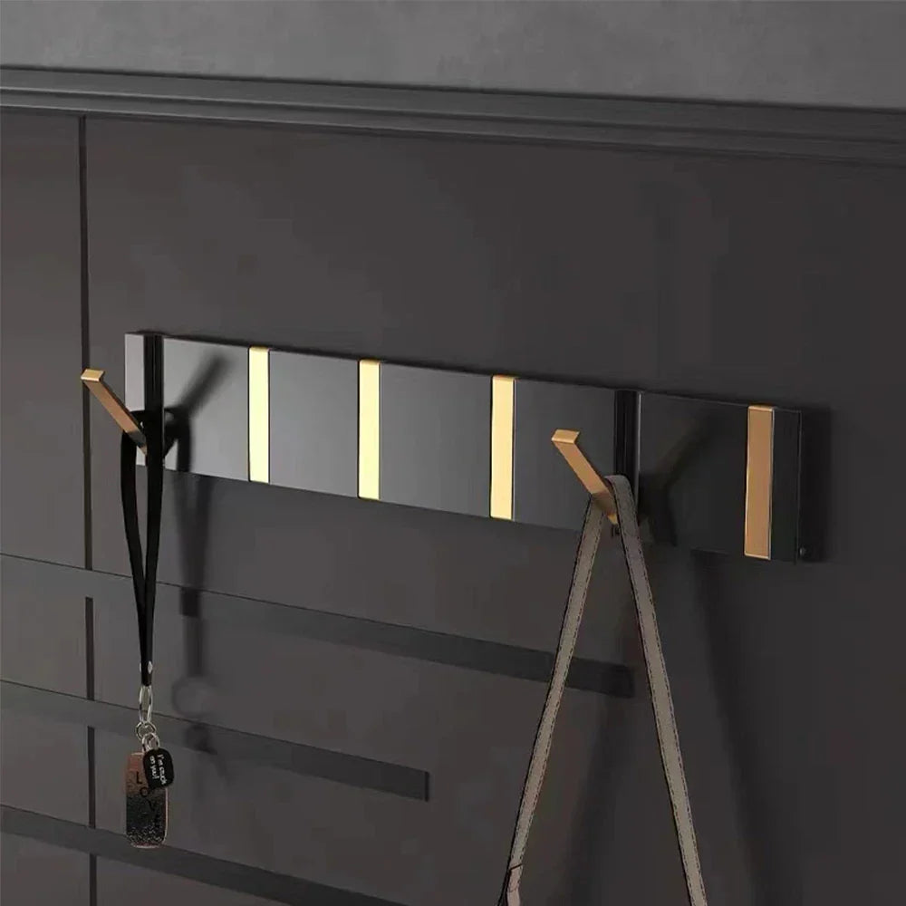Black wall-mounted coat rack with gold accents on a dark gray wall.