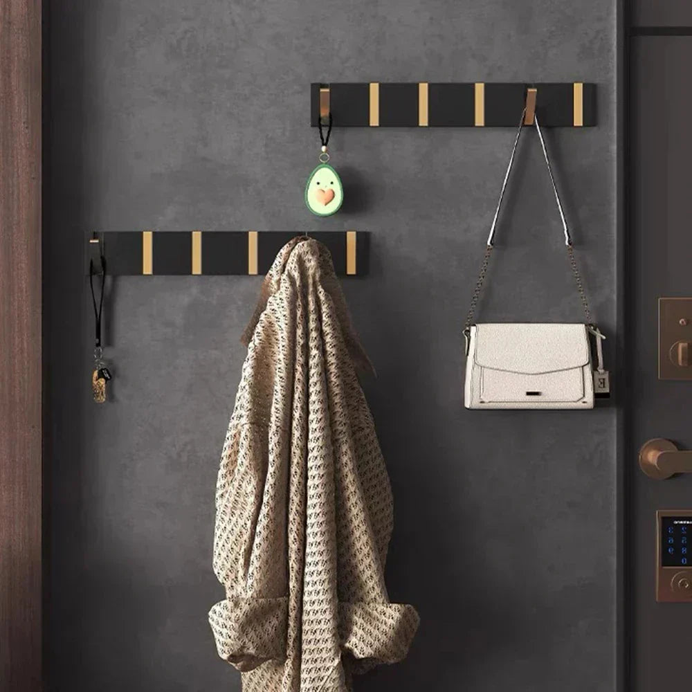 Wall-mounted coat rack with hooks holding a coat, handbag, and small green object on a gray wall.