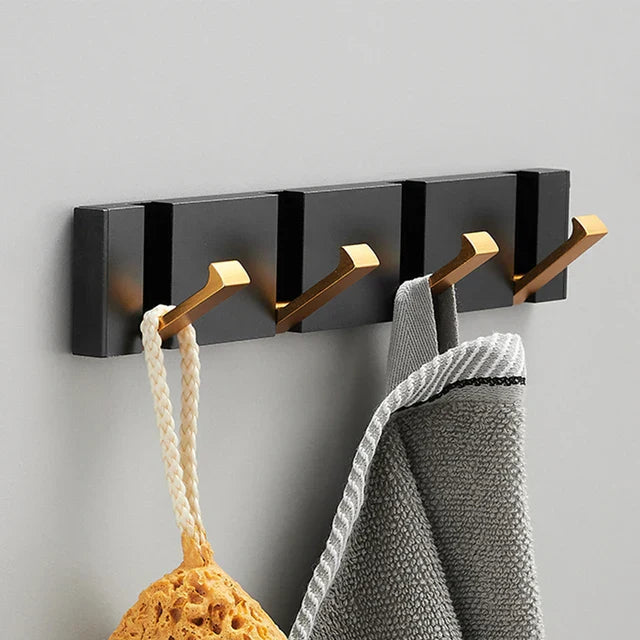 Black wall-mounted hook with gold hooks holding a sponge and a towel on a gray background