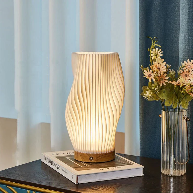 Table lamp with wavy design on a book next to a vase with flowers, against a curtain background