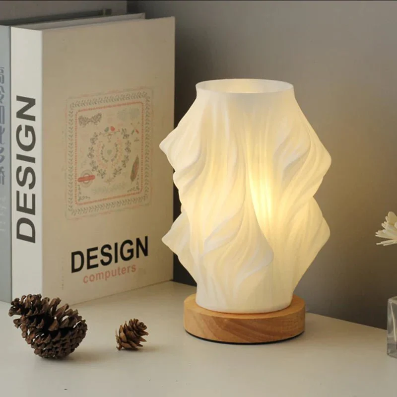 Decorative lamp with wavy design on a wooden base next to a book titled 'Design Computers'.