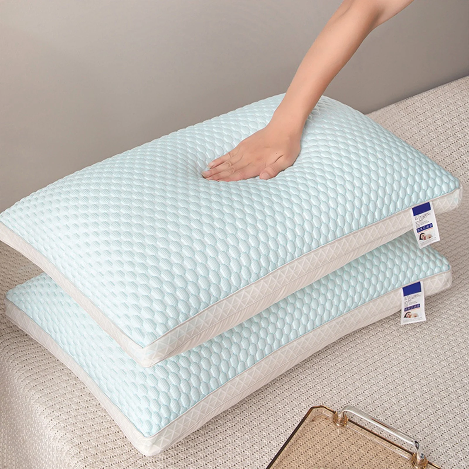 Two light blue pillows on a beige surface with a hand touching one of them.