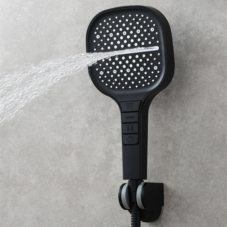 Black handheld shower head with water spraying against a gray concrete wall