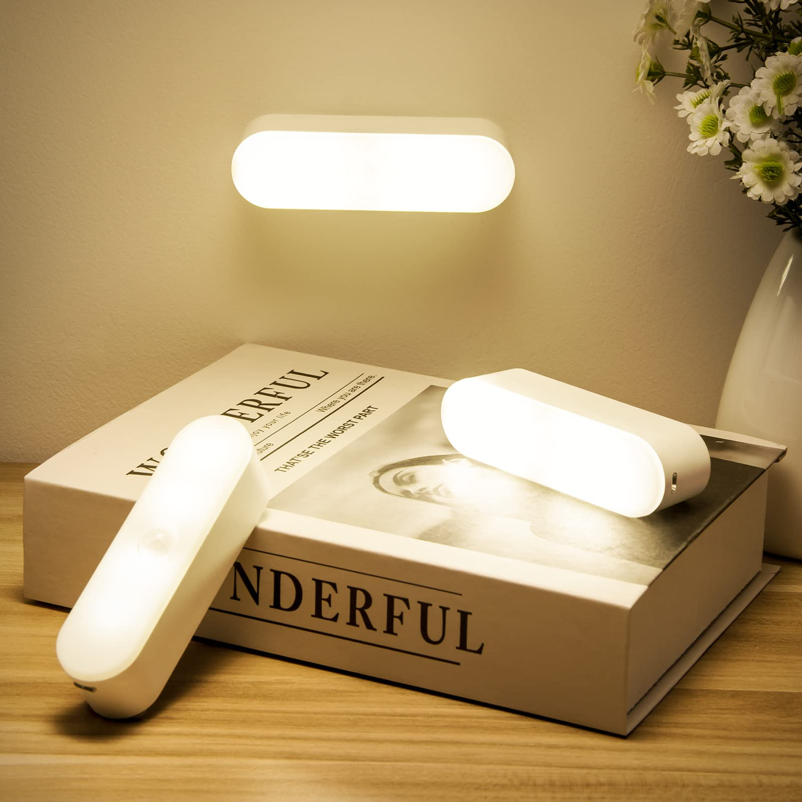 Modern wall-mounted and table lamp on a book with 'WONDERFUL' text, illuminated in a warm setting.