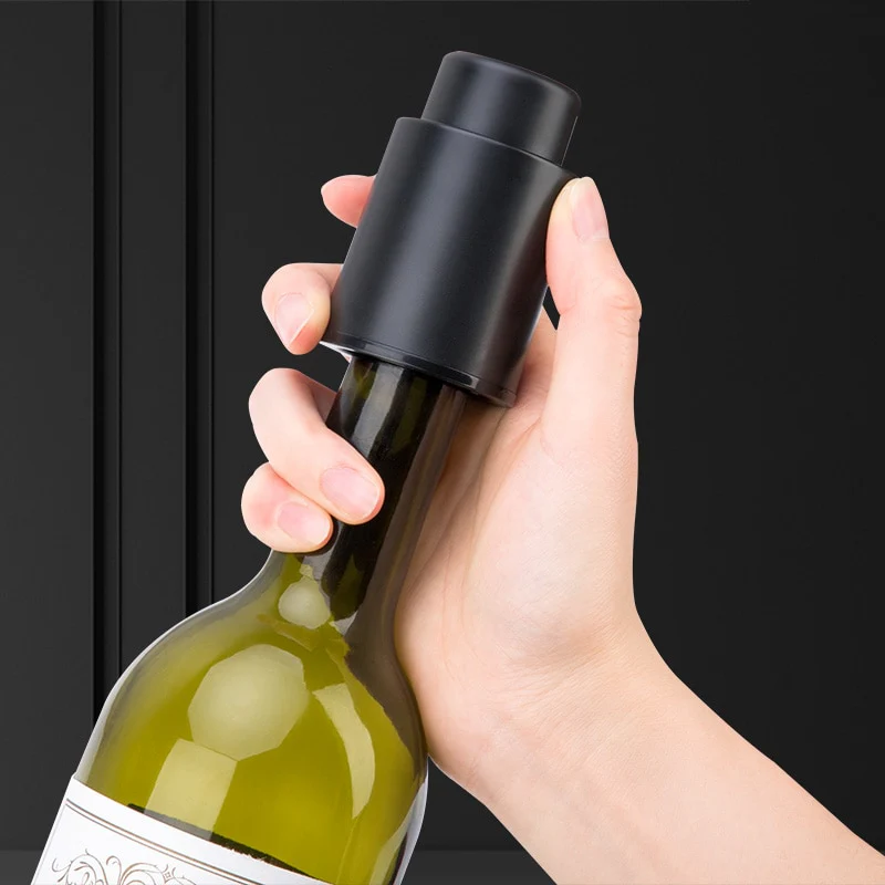 Hand holding a wine bottle with a black wine stopper against a dark background
