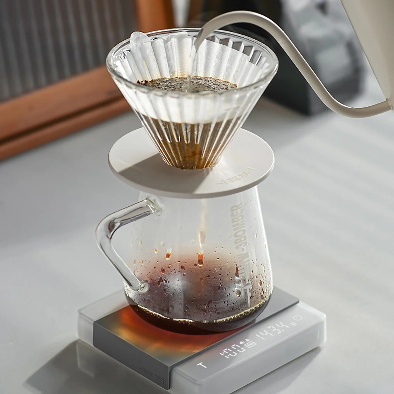 Coffee brewing process using a glass carafe and filter on a white surface.