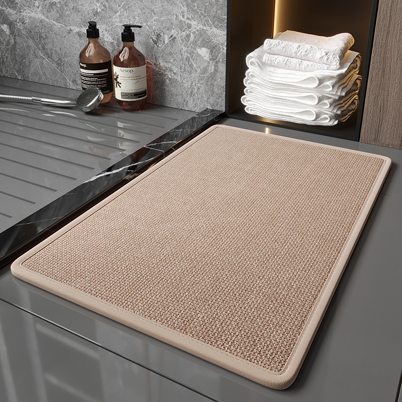 Beige bath mat on a bathroom floor with towels and bottles in the background