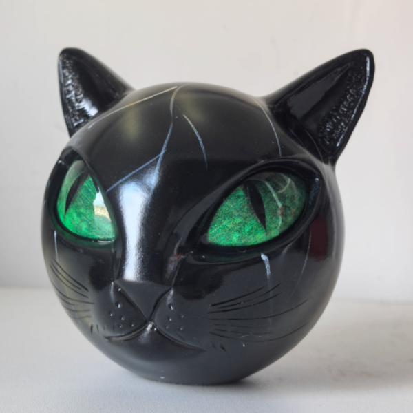 Black cat-shaped object with green eyes on a white background