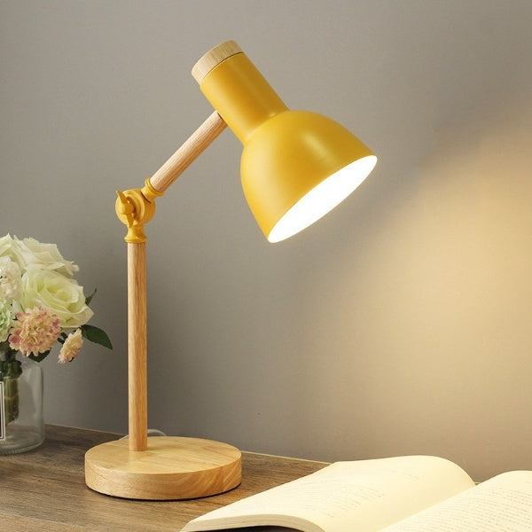 Yellow desk lamp on a wooden base with a soft glow, placed on a surface with a blurred background.