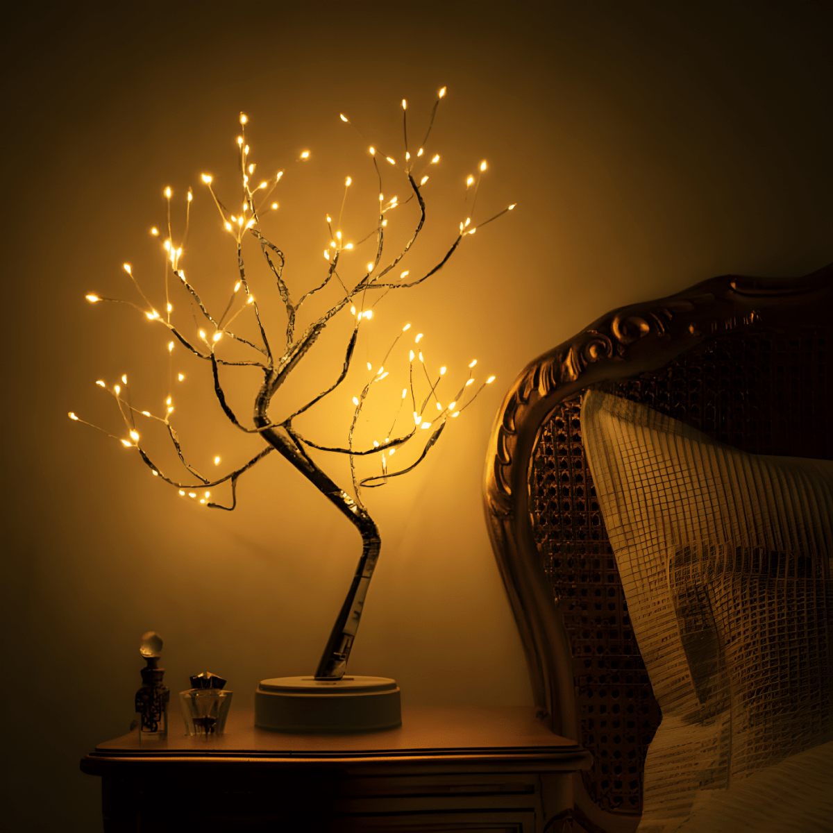 Decorative lighted branch on a table next to a chair with a warm glow.