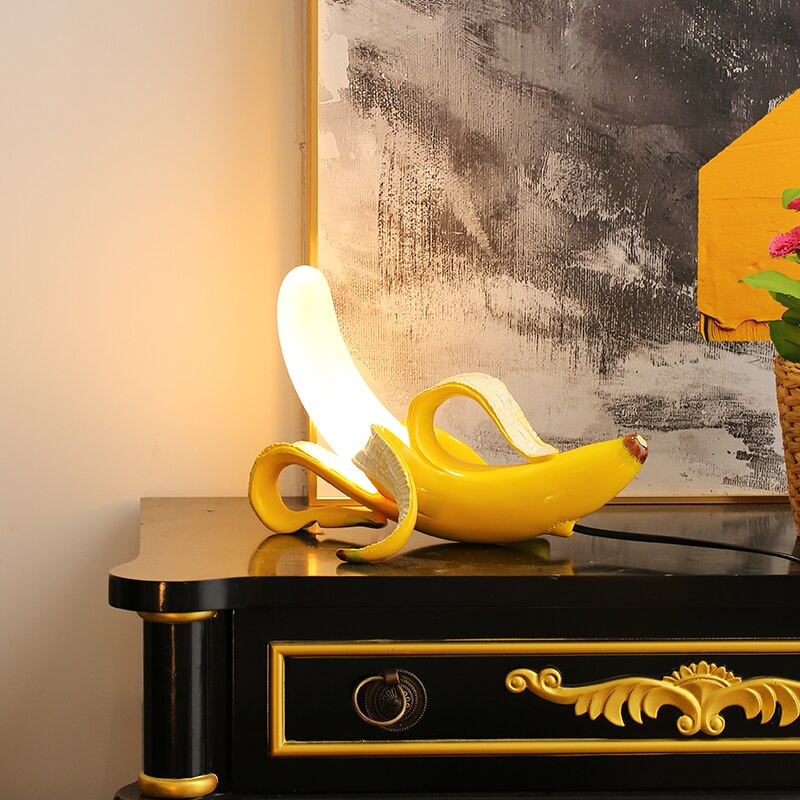 Decorative banana sculpture on a black and gold console table with abstract art in the background.