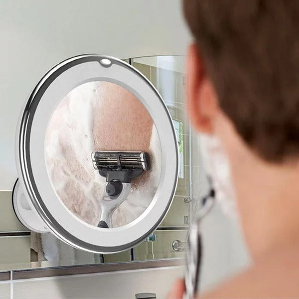 Person shaving with a razor in front of a magnifying mirror with lights.