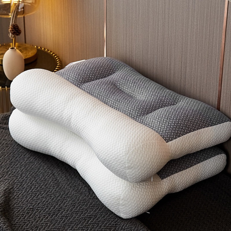 Two ergonomic pillows stacked on a bed with a lamp in the background.