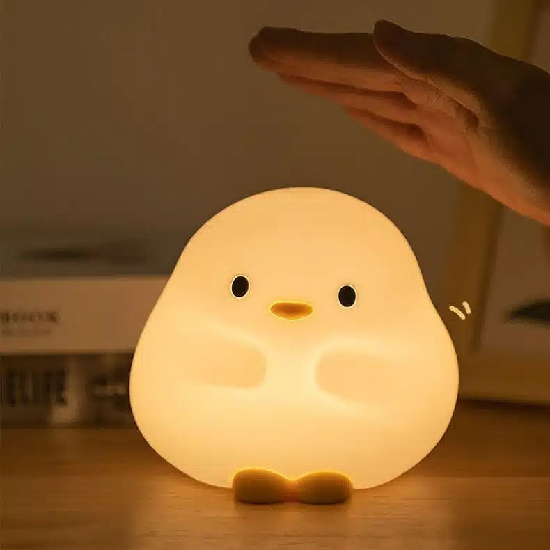 Cute chick-shaped night light being held by a hand on a wooden surface.
