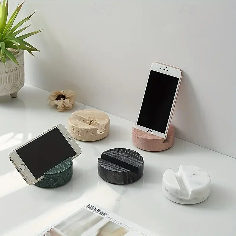 Four different phone stands on a white surface with a plant and magazine in the background.