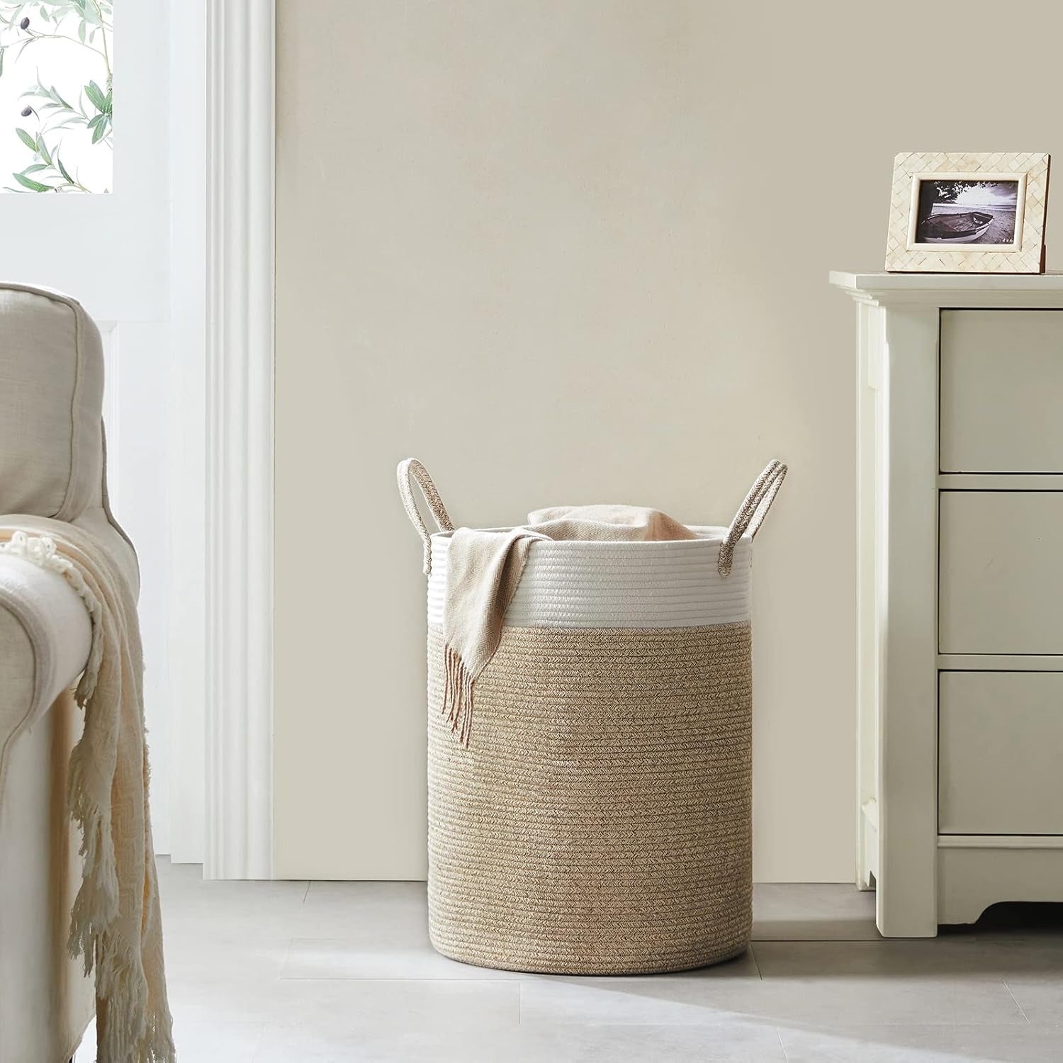 Beige woven laundry basket with a white interior in a room with a beige wall and white furniture.