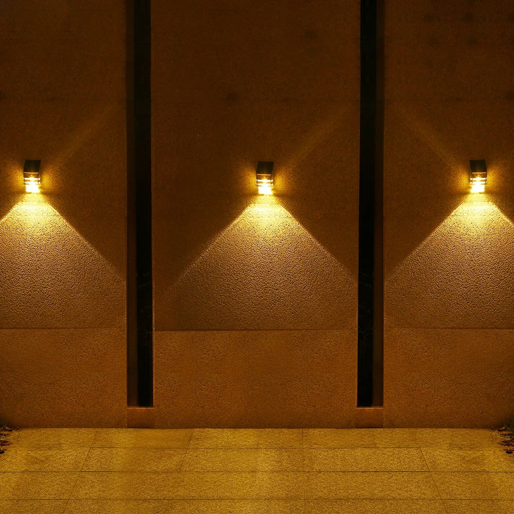 Three wall-mounted lights on a textured wall casting shadows on a tiled floor.