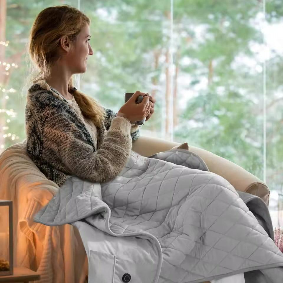 Woman sitting on a couch with a blanket and holding a mug, surrounded by greenery.