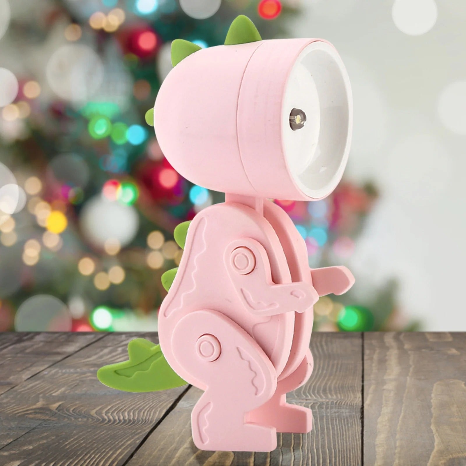 Pink dinosaur-shaped lamp on a wooden surface with a blurred festive background
