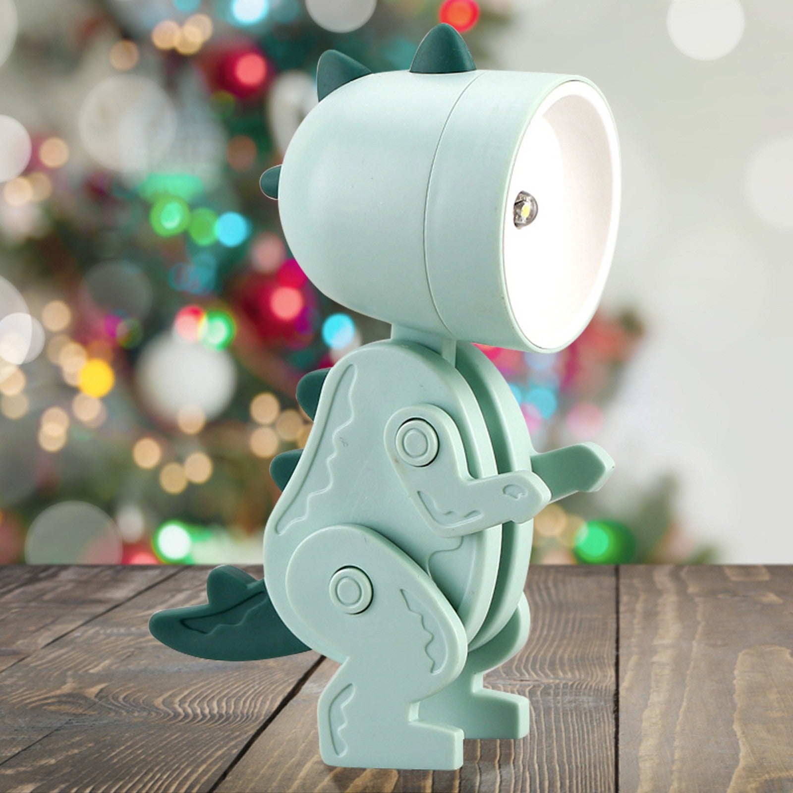 Light blue dinosaur-shaped lamp on a wooden surface with a blurred festive background