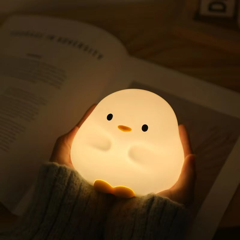 Hand holding a chick-shaped night light with an open book in the background