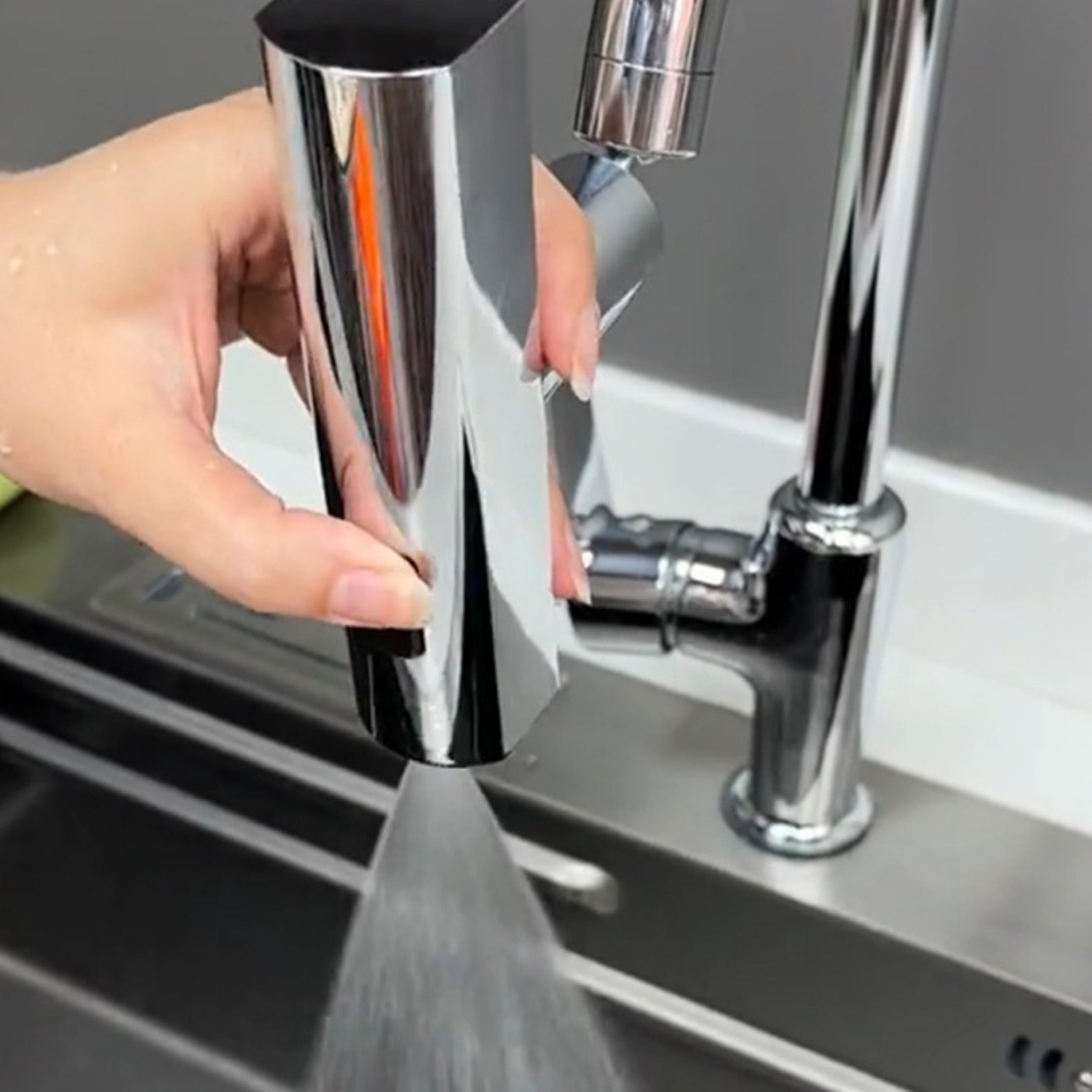 Hand holding a metallic faucet handle with water flowing, set against a kitchen sink background.