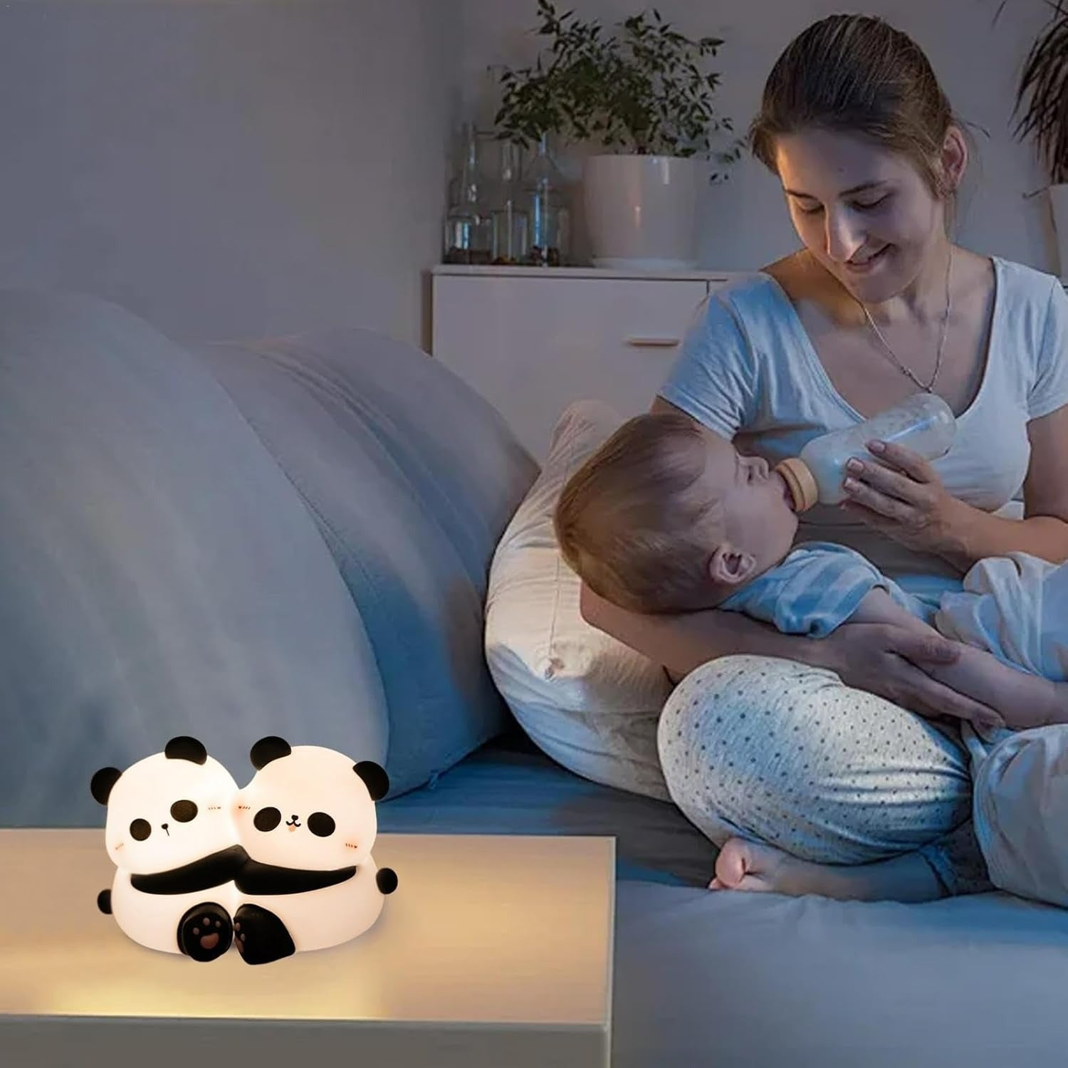 Woman feeding a baby with a bottle in a cozy room, next to two panda-shaped night lights.