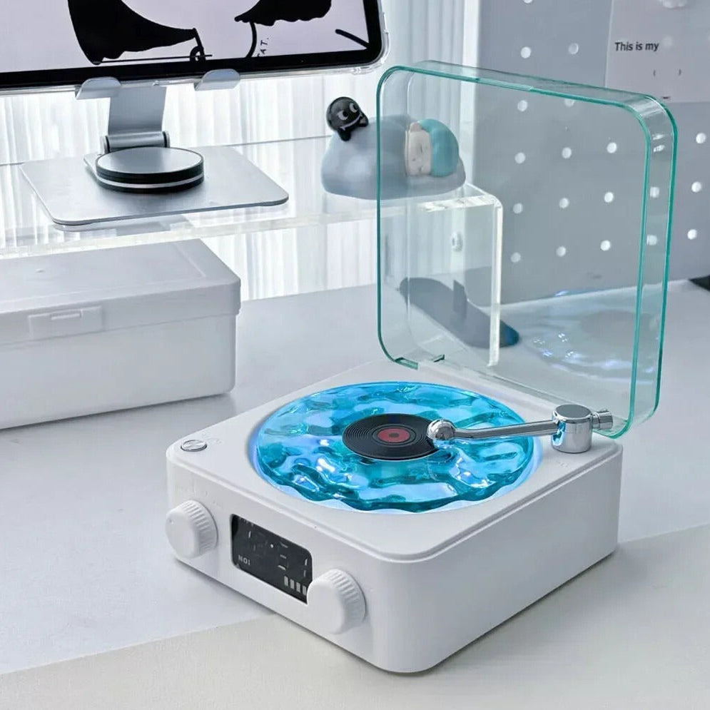 Modern record player with a transparent turntable on a white surface, with a computer monitor in the background.