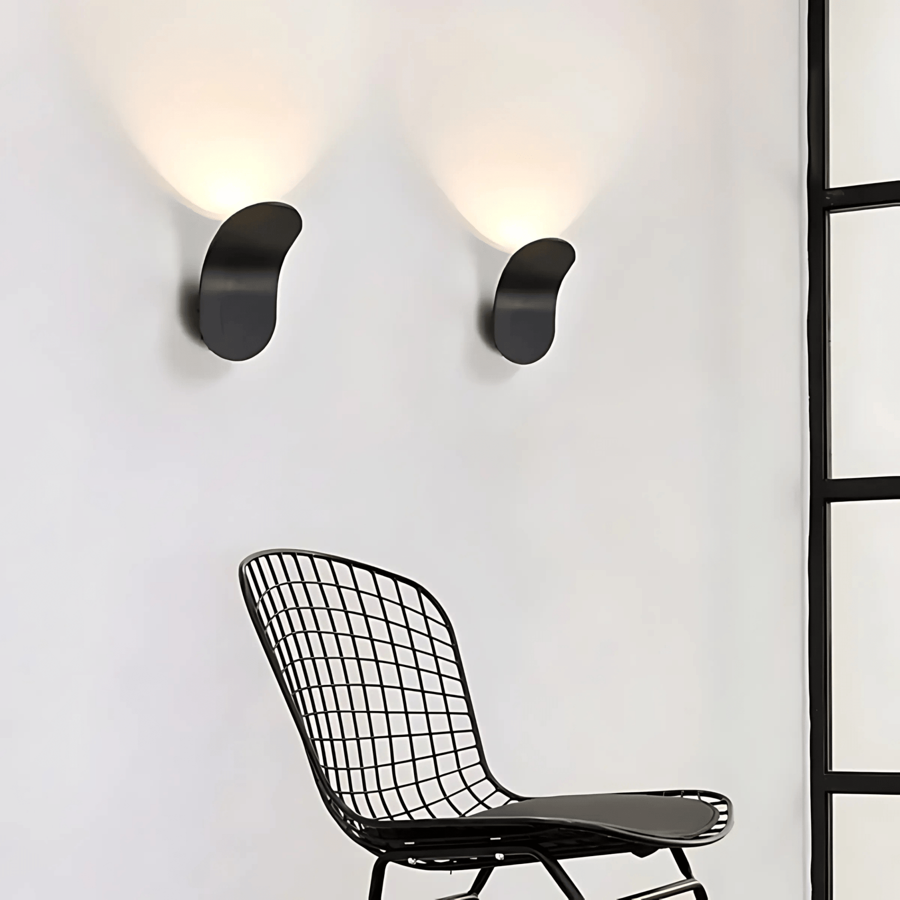 Modern black wire chair in front of a white wall with two wall-mounted lights.