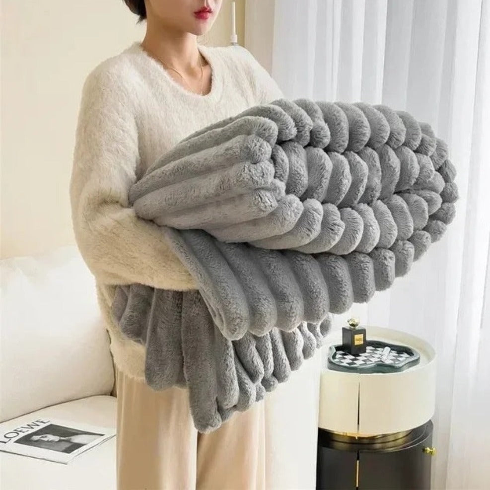 Person holding a large gray textured blanket in a room with a couch and coffee table.