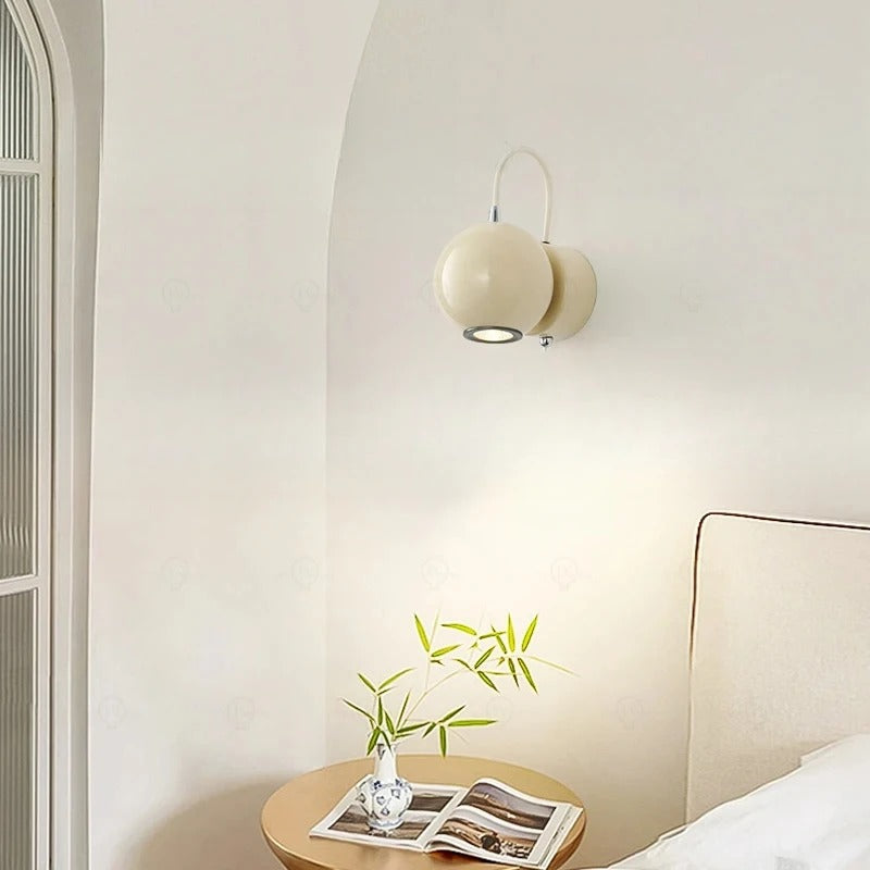 Wall-mounted light fixture in a bedroom with a small plant and open magazine on a nightstand.