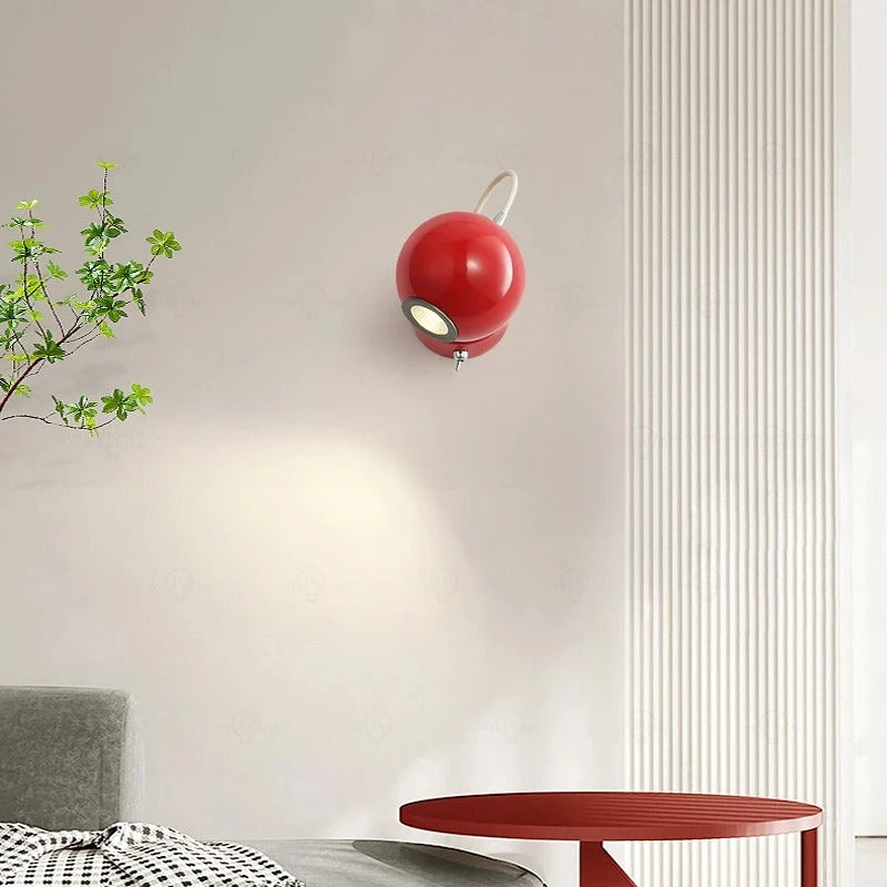 Red wall lamp on a light gray wall with a plant and table in the foreground