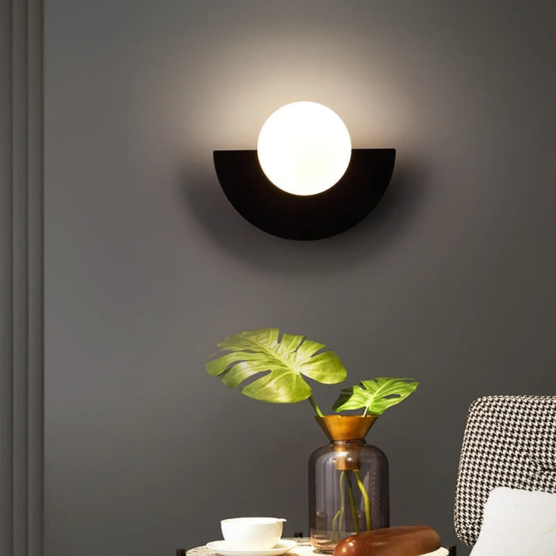 Wall-mounted light fixture on a dark gray wall with a plant and decorative items below.
