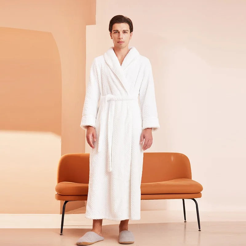 Man wearing a white robe standing in a minimalistic room with a brown chair.